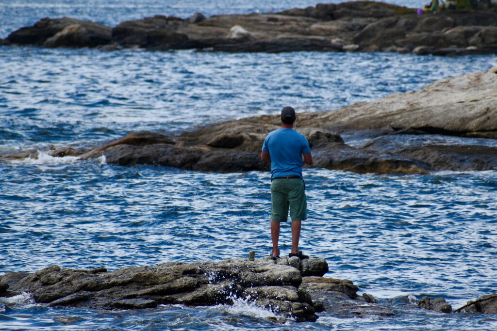 Hombre pescando en la costa desde rocas en verano